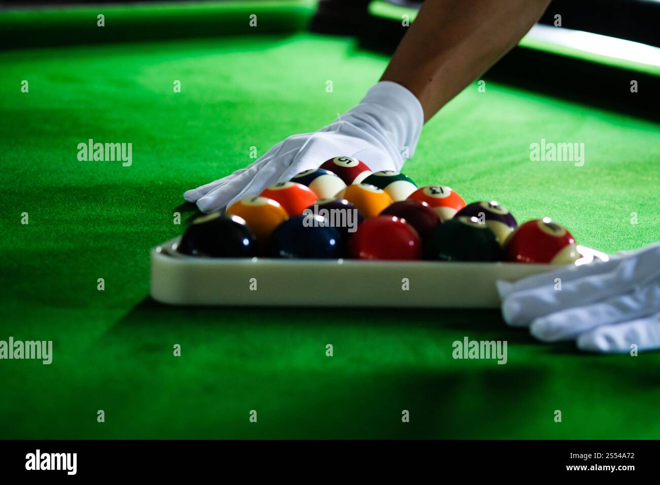 Mans mano e braccio cue giocano a biliardo o si preparano a sparare palle da biliardo su un tavolo da biliardo verde. Palline da biliardo colorate sul fregio verde Foto Stock