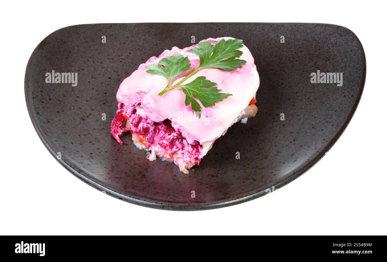 Porzione di insalata russa di aringhe vestita decorata con foglie di prezzemolo su piatto nero isolato su sfondo bianco. Porzione di aringhe vestite di russo Foto Stock