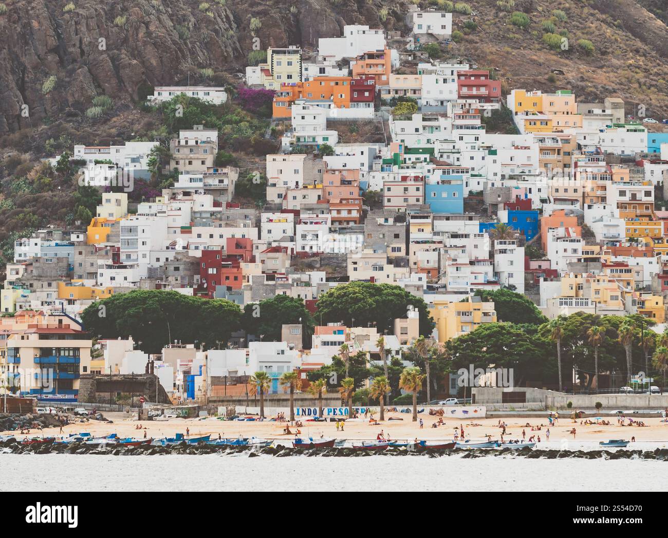 Foto tonificata di una bellissima cittadina con edifici colorati tra le montagne alte e la spiaggia dell'oceano, Tenerife, Spagna. Immagine dai colori vivaci di piccole dimensioni Foto Stock