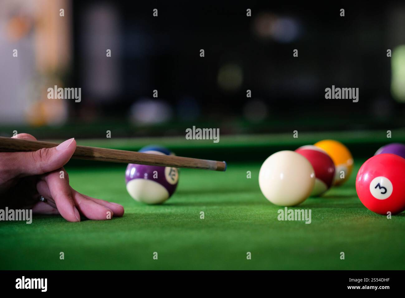 Mans mano e braccio cue giocano a biliardo o si preparano a sparare palle da biliardo su un tavolo da biliardo verde. Palline da biliardo colorate sul fregio verde Foto Stock