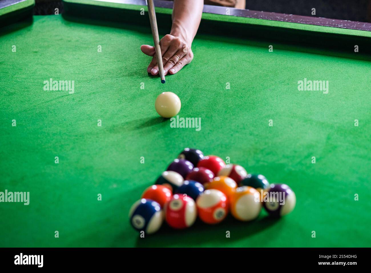 Mans mano e braccio cue giocano a biliardo o si preparano a sparare palle da biliardo su un tavolo da biliardo verde. Palline da biliardo colorate sul fregio verde Foto Stock