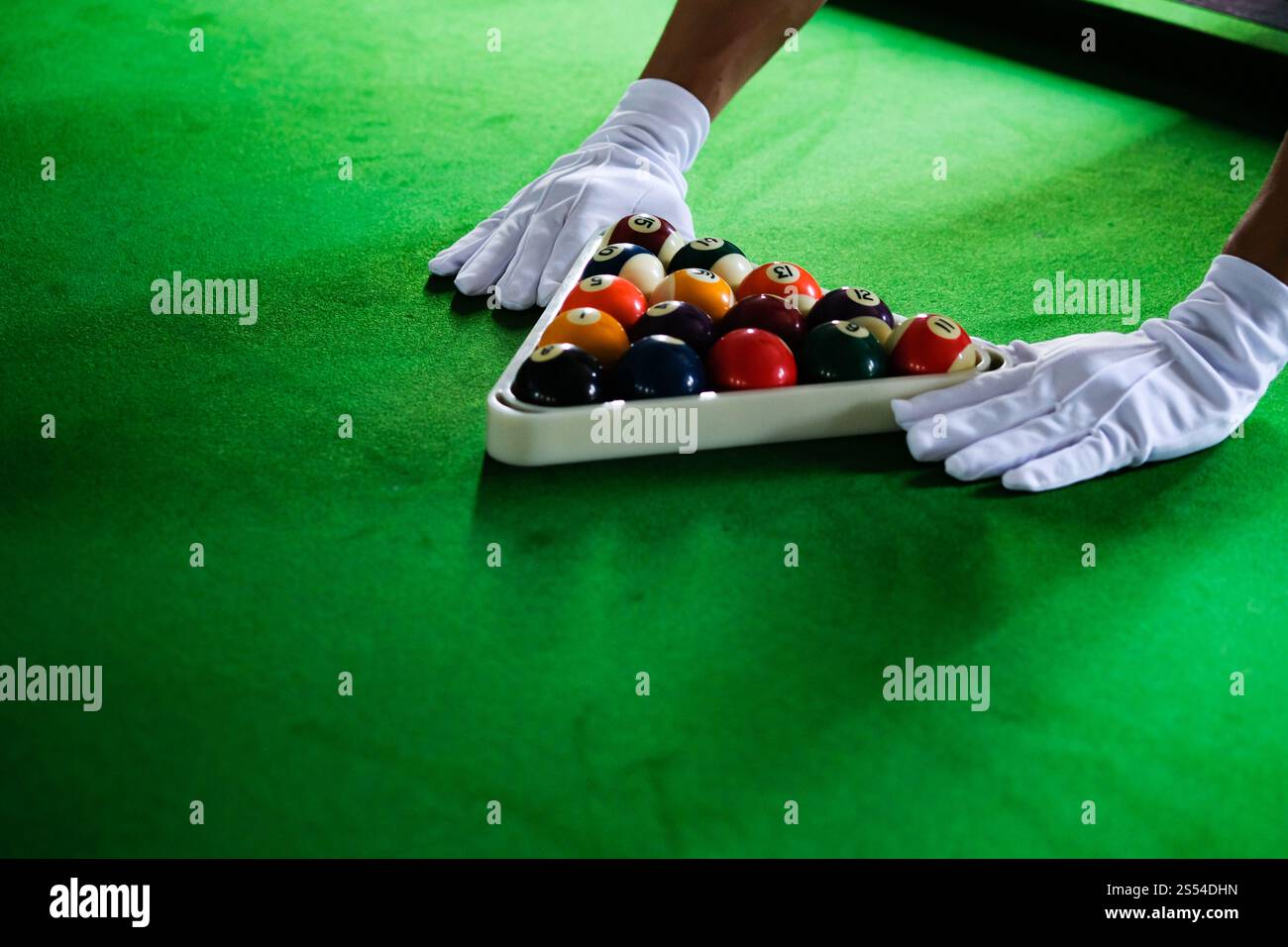 Mans mano e braccio cue giocano a biliardo o si preparano a sparare palle da biliardo su un tavolo da biliardo verde. Palline da biliardo colorate sul fregio verde Foto Stock