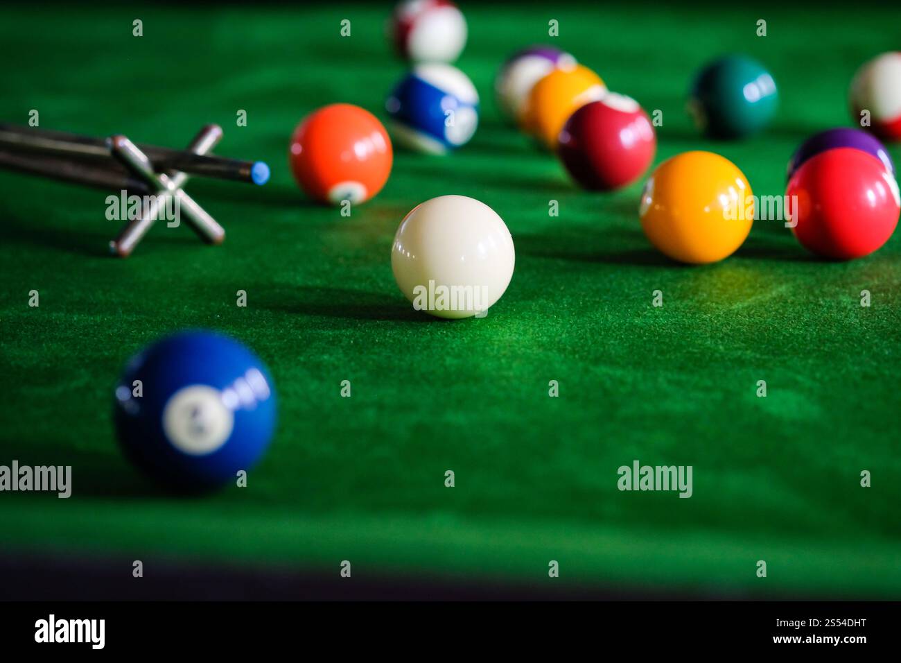 Mans mano e braccio cue giocano a biliardo o si preparano a sparare palle da biliardo su un tavolo da biliardo verde. Palline da biliardo colorate sul fregio verde Foto Stock