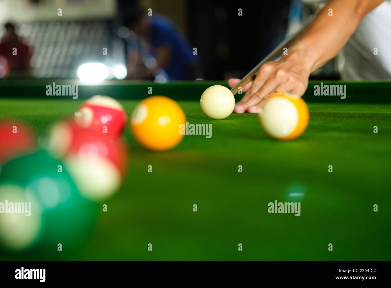 Mans mano e braccio cue giocano a biliardo o si preparano a sparare palle da biliardo su un tavolo da biliardo verde. Palline da biliardo colorate sul fregio verde Foto Stock