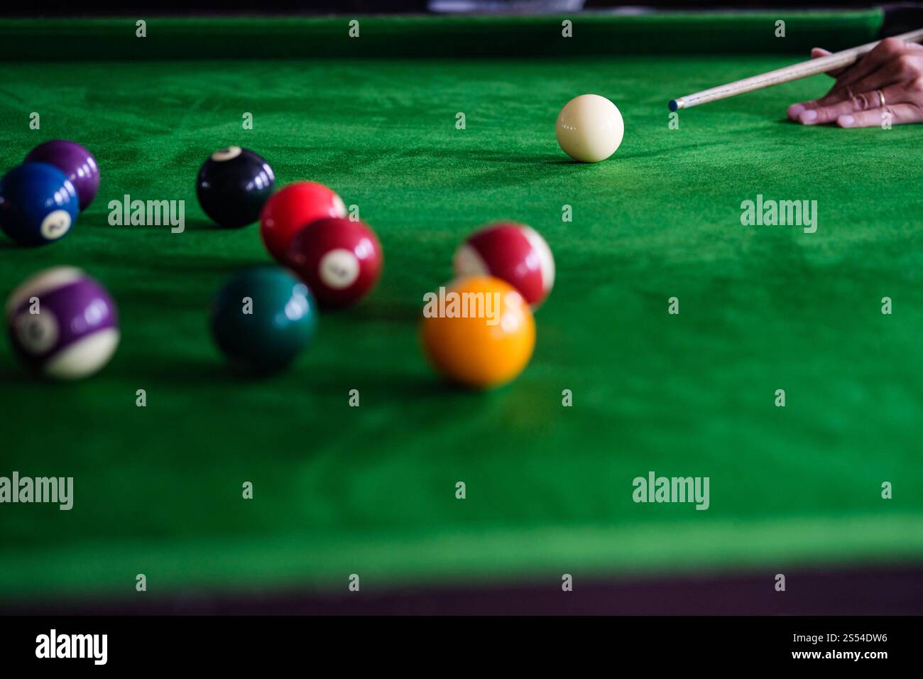 Mans mano e braccio cue giocano a biliardo o si preparano a sparare palle da biliardo su un tavolo da biliardo verde. Palline da biliardo colorate sul fregio verde Foto Stock