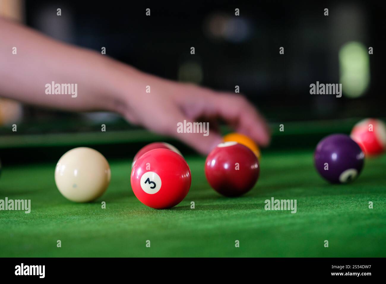 Mans mano e braccio cue giocano a biliardo o si preparano a sparare palle da biliardo su un tavolo da biliardo verde. Palline da biliardo colorate sul fregio verde Foto Stock
