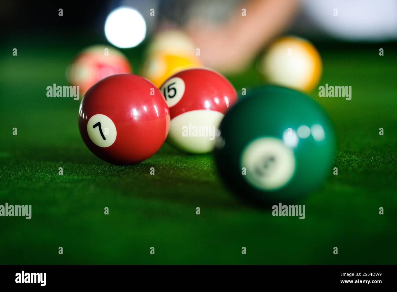 Mans mano e braccio cue giocano a biliardo o si preparano a sparare palle da biliardo su un tavolo da biliardo verde. Palline da biliardo colorate sul fregio verde Foto Stock