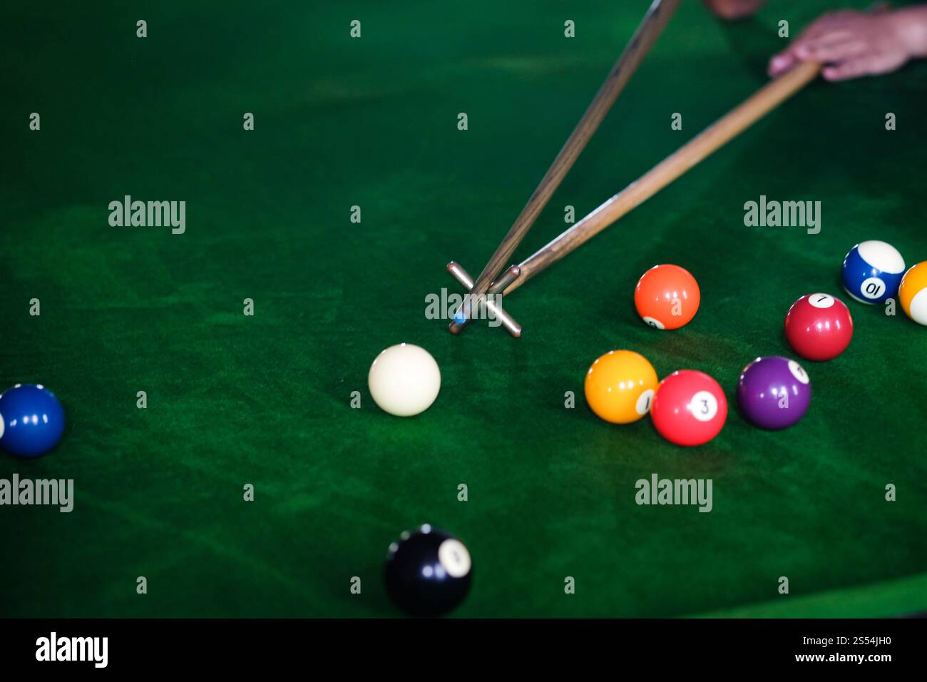 Mans mano e braccio cue giocano a biliardo o si preparano a sparare palle da biliardo su un tavolo da biliardo verde. Palline da biliardo colorate sul fregio verde Foto Stock