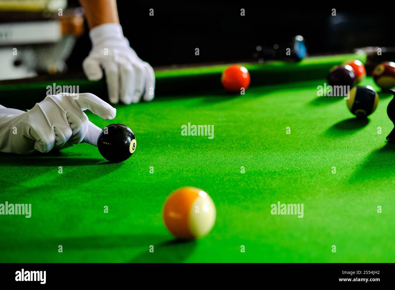 Mans mano e braccio cue giocano a biliardo o si preparano a sparare palle da biliardo su un tavolo da biliardo verde. Palline da biliardo colorate sul fregio verde Foto Stock