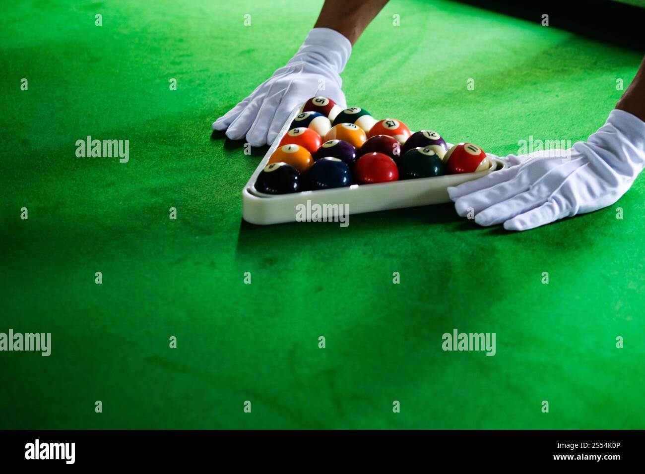 Mans mano e braccio cue giocano a biliardo o si preparano a sparare palle da biliardo su un tavolo da biliardo verde. Palline da biliardo colorate sul fregio verde Foto Stock