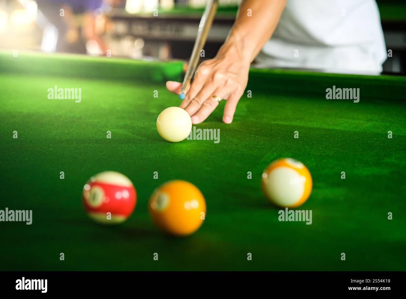 Mans mano e braccio cue giocano a biliardo o si preparano a sparare palle da biliardo su un tavolo da biliardo verde. Palline da biliardo colorate sul fregio verde Foto Stock