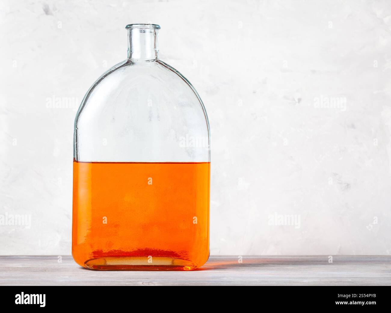 matraccio di vetro con soluzione acquerello arancione su un pannello di legno grigio vicino alla parete di cemento grigio. matraccio con soluzione acquerello arancione su grigio Foto Stock