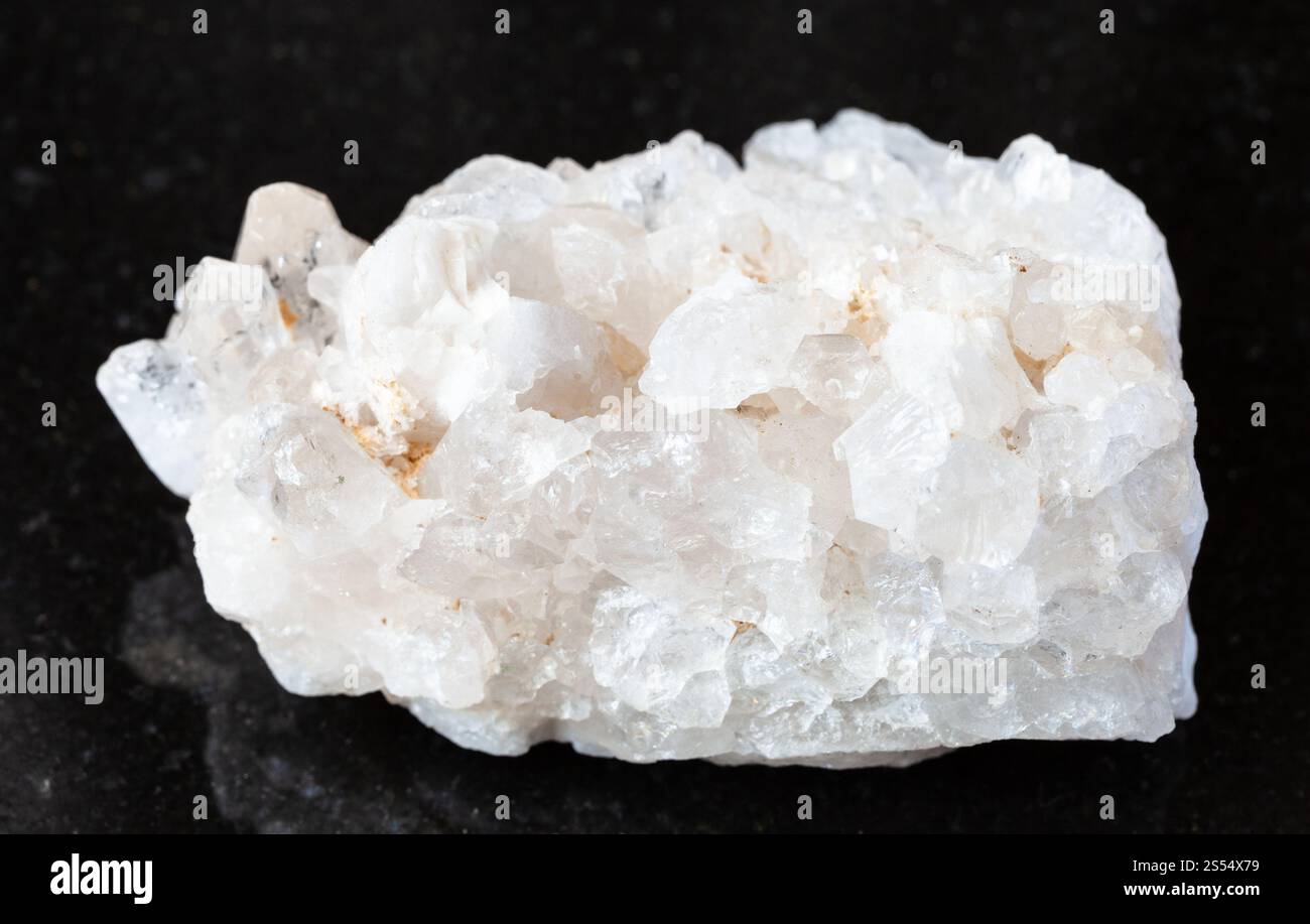 primo piano di un campione di minerale naturale proveniente dalla collezione geologica - druso non lucidato di cristalli di roccia incolore (cristallo di roccia) su granito nero Foto Stock