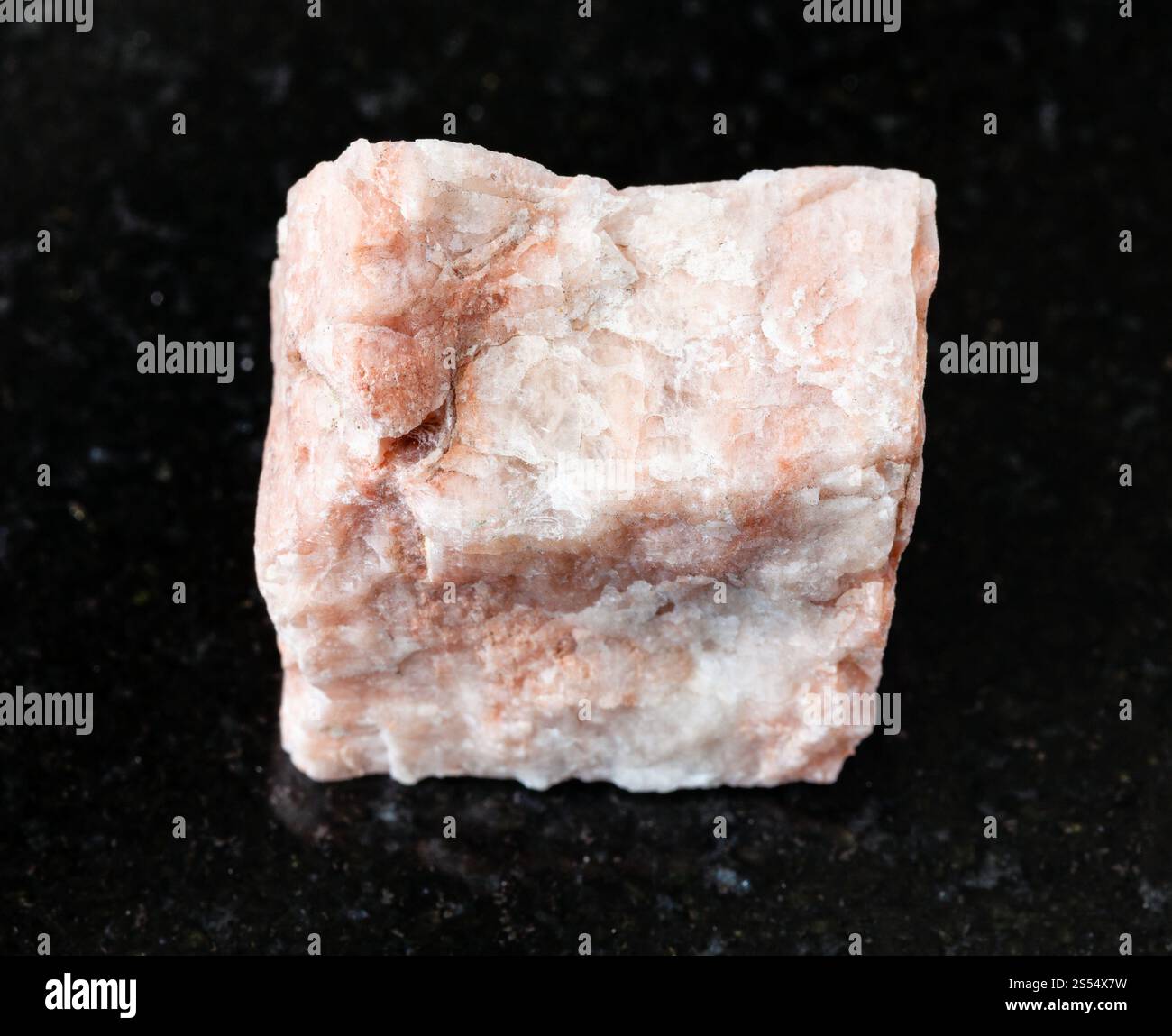 primo piano di un campione di minerale naturale proveniente dalla collezione geologica - roccia Feldspar non lucidata su fondo di granito nero. Roccia Feldspar non lucidata Foto Stock