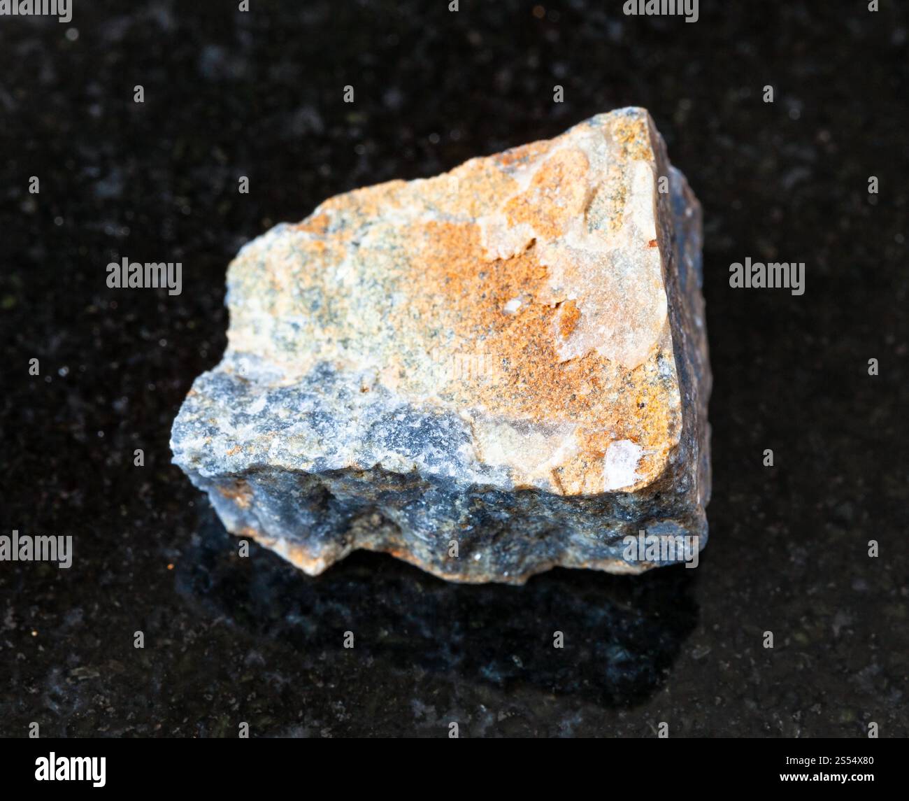 primo piano di un campione di minerale naturale proveniente dalla collezione geologica - roccia di corindone non lucidata su fondo di granito nero. Corindone non lucidato acceso Foto Stock