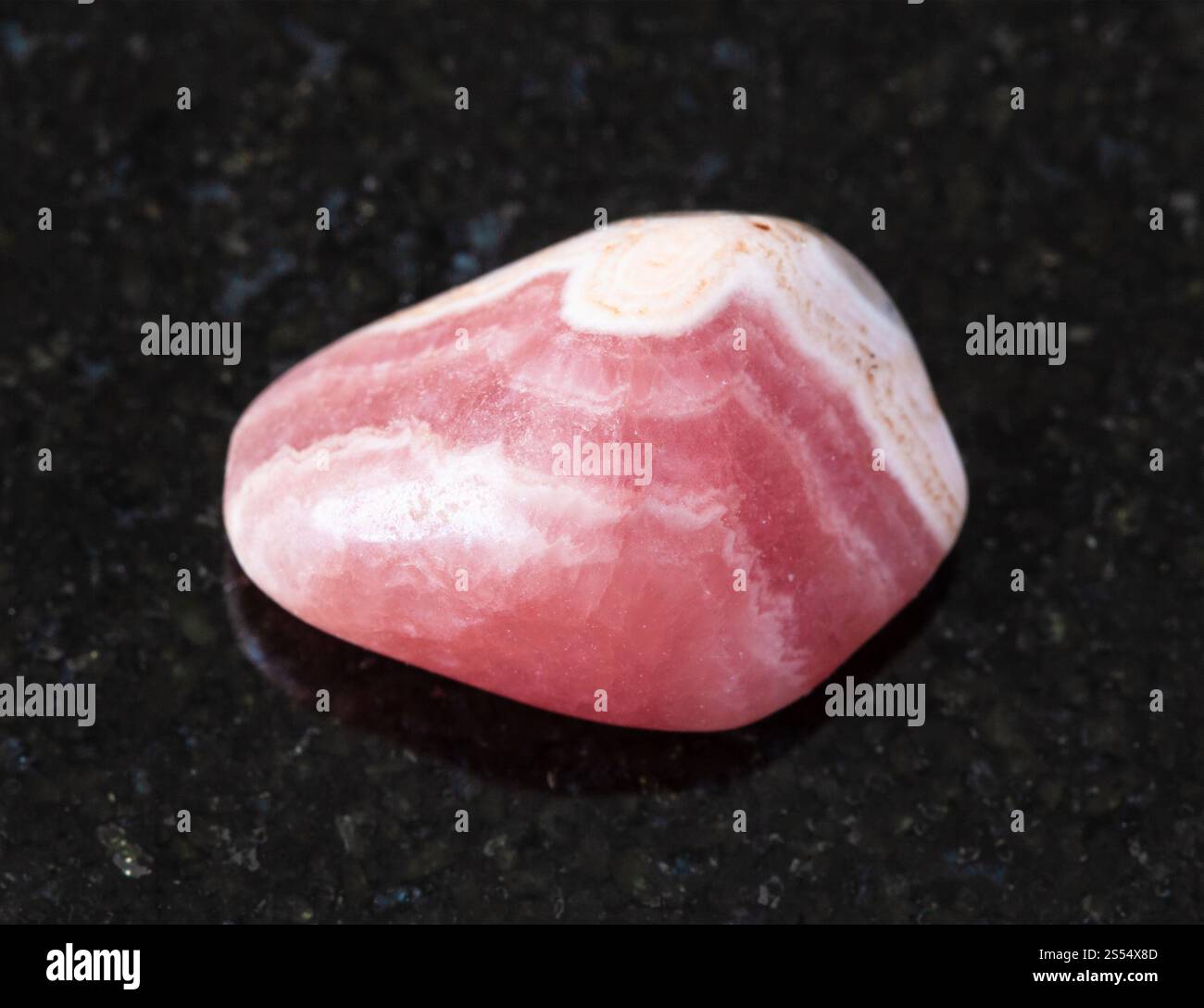 primo piano di un campione di minerale naturale proveniente dalla collezione geologica - roccia rodocrosita lucidata su fondo di granito nero proveniente dall'Argentina. lucidato Foto Stock