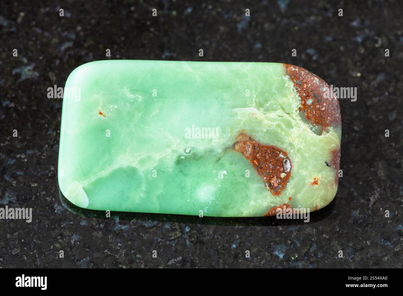 primo piano di un campione di minerale naturale proveniente dalla raccolta geologica - roccia Chrysoprase tumulata su fondo di granito nero proveniente da Newman, Australia. Foto Stock
