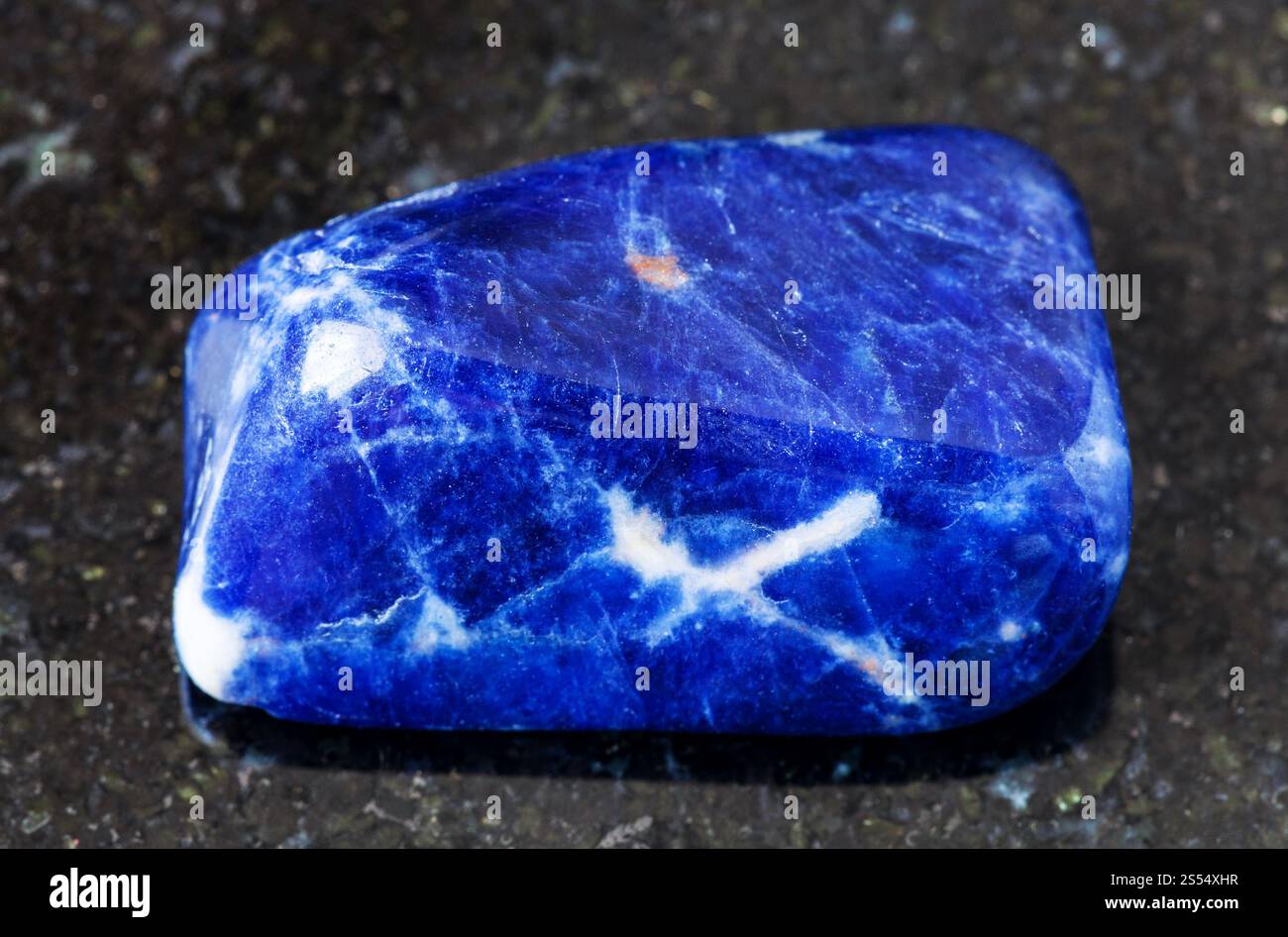 primo piano di un campione di minerale naturale proveniente dalla collezione geologica - roccia di Sodalite lucidata su fondo di granito nero proveniente dal Brasile. Sodalite lucido Foto Stock