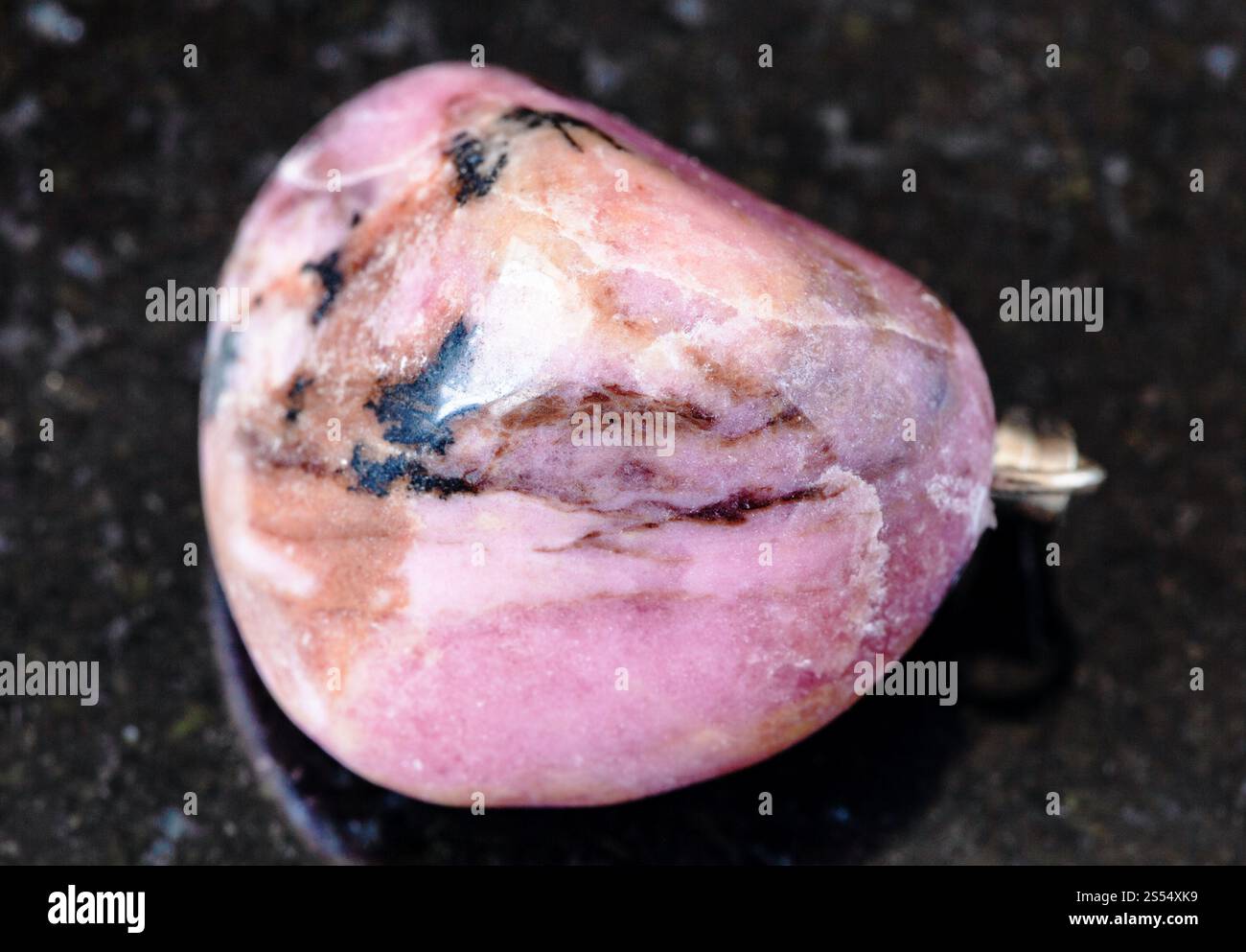 primo piano di un campione di minerale naturale proveniente dalla collezione geologica - roccia rodonita arrotolata su fondo di granito nero proveniente dal Tagikistan. Rodonite arrotolata Foto Stock