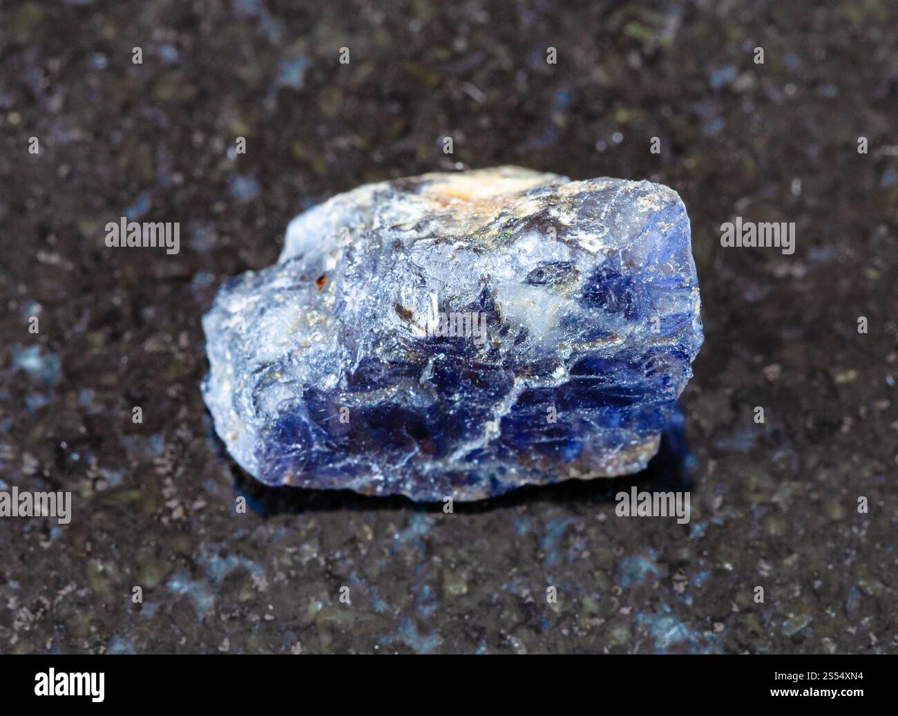 primo piano di un campione di minerale naturale proveniente dalla raccolta geologica - cristallo di cordierite ruvida (Iolite) su fondo di granito nero del Madagascar. Foto Stock