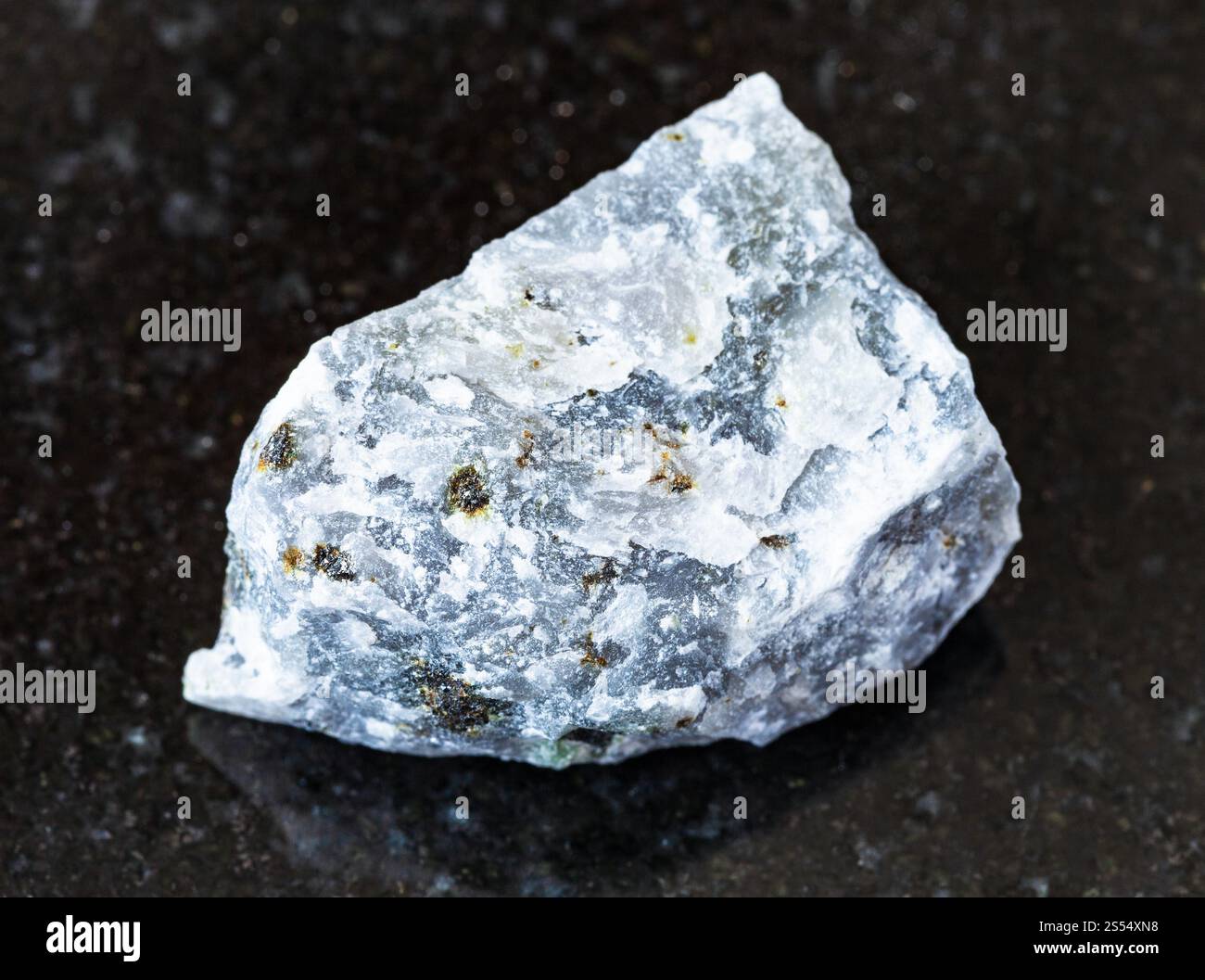 primo piano di un campione di minerale naturale proveniente dalla collezione geologica - roccia grezza di Melilitolite su fondo di granito nero. Ruvida roccia Melilitolite Foto Stock