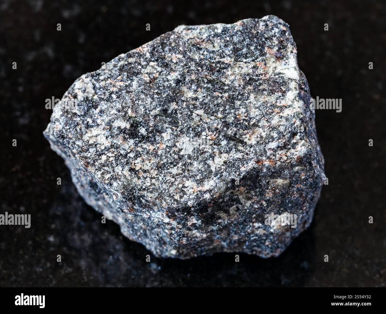 primo piano di un campione di minerale naturale proveniente dalla raccolta geologica - roccia di sienite Nepheline ruvida su fondo di granito nero. Sienite Nepheline ruvida Foto Stock