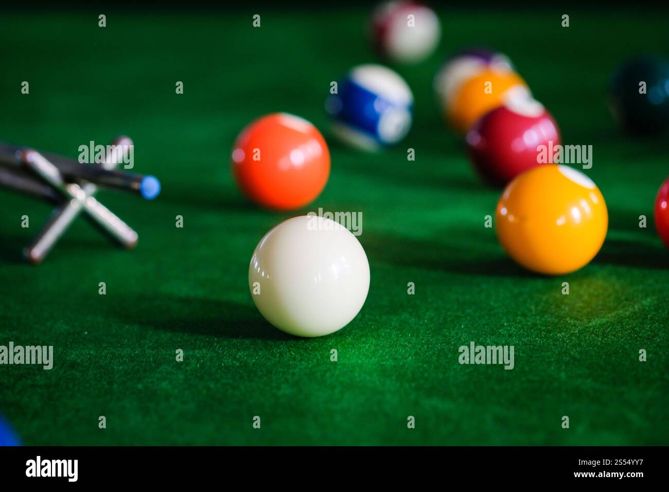 Mans mano e braccio cue giocano a biliardo o si preparano a sparare palle da biliardo su un tavolo da biliardo verde. Palline da biliardo colorate sul fregio verde Foto Stock