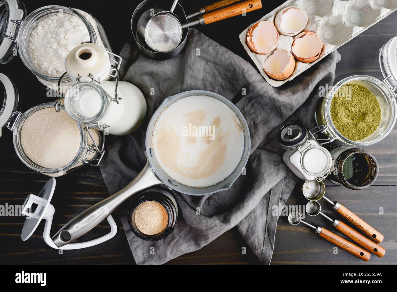 Prova del lievito nel latte riscaldato in una pentola piccola: Direttamente sopra il lievito protetto nel latte circondato da altri ingredienti del pane e utensili da cucina Foto Stock