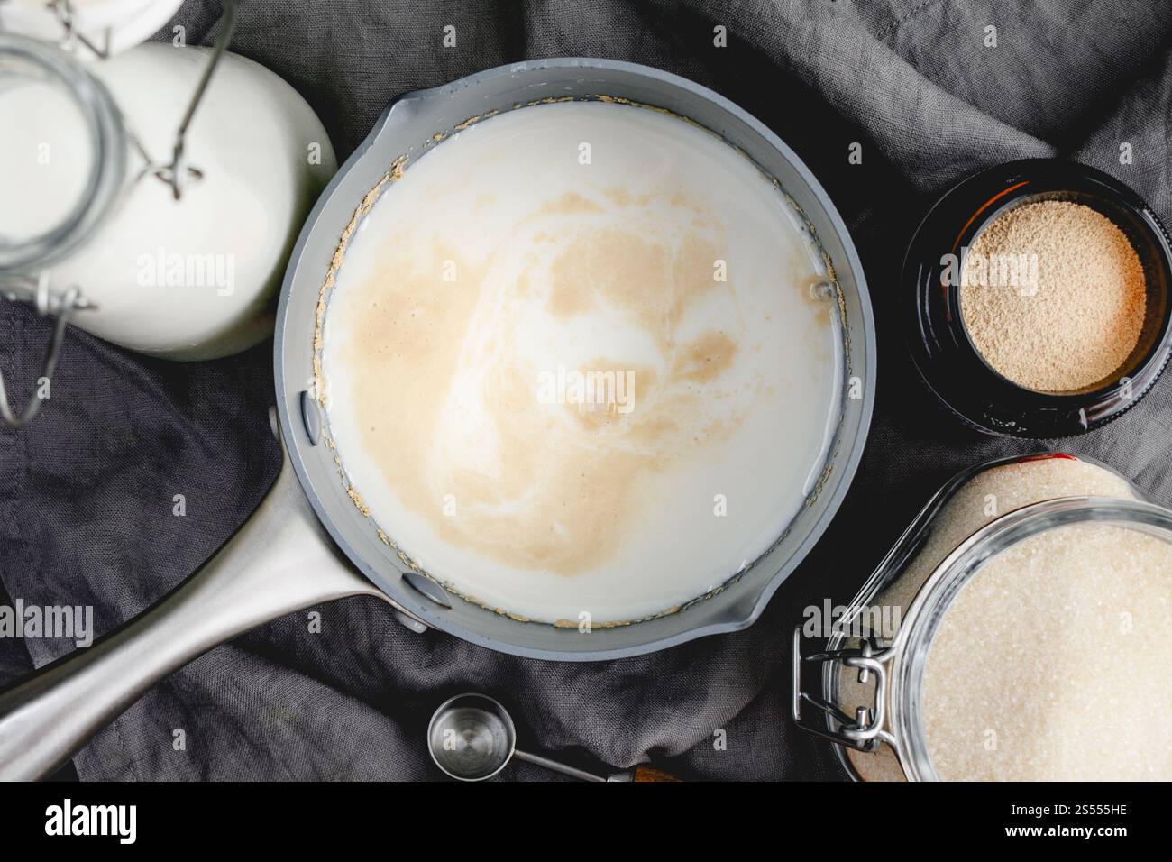 Vista ravvicinata della prova del lievito nel latte riscaldato: Direttamente sopra il lievito protetto in una pentola con altri ingredienti per il pane e utensili da cucina Foto Stock