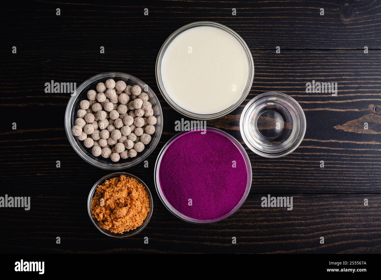 Ingredienti per il tè Bubble Purple Sweet Potato: Patate dolci in polvere, polpette di tapioca e altri ingredienti su un tavolo di legno scuro Foto Stock