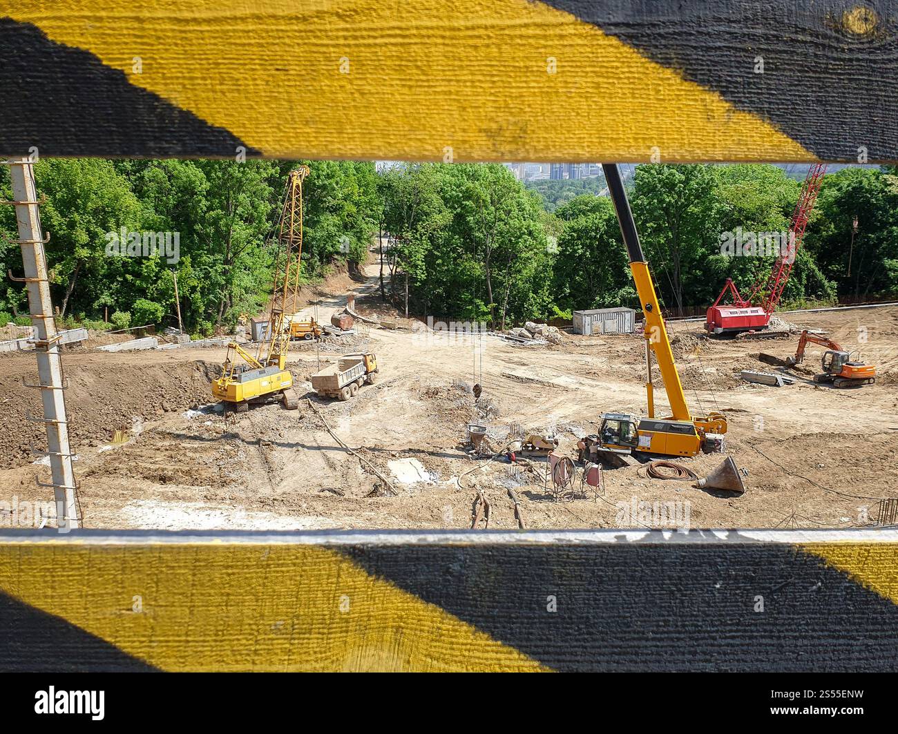 Foto di macchinari pesanti per l'edilizia che lavorano nel cantiere dietro la recinzione protettiva. Immagine di macchinari pesanti per l'edilizia che lavorano su Foto Stock