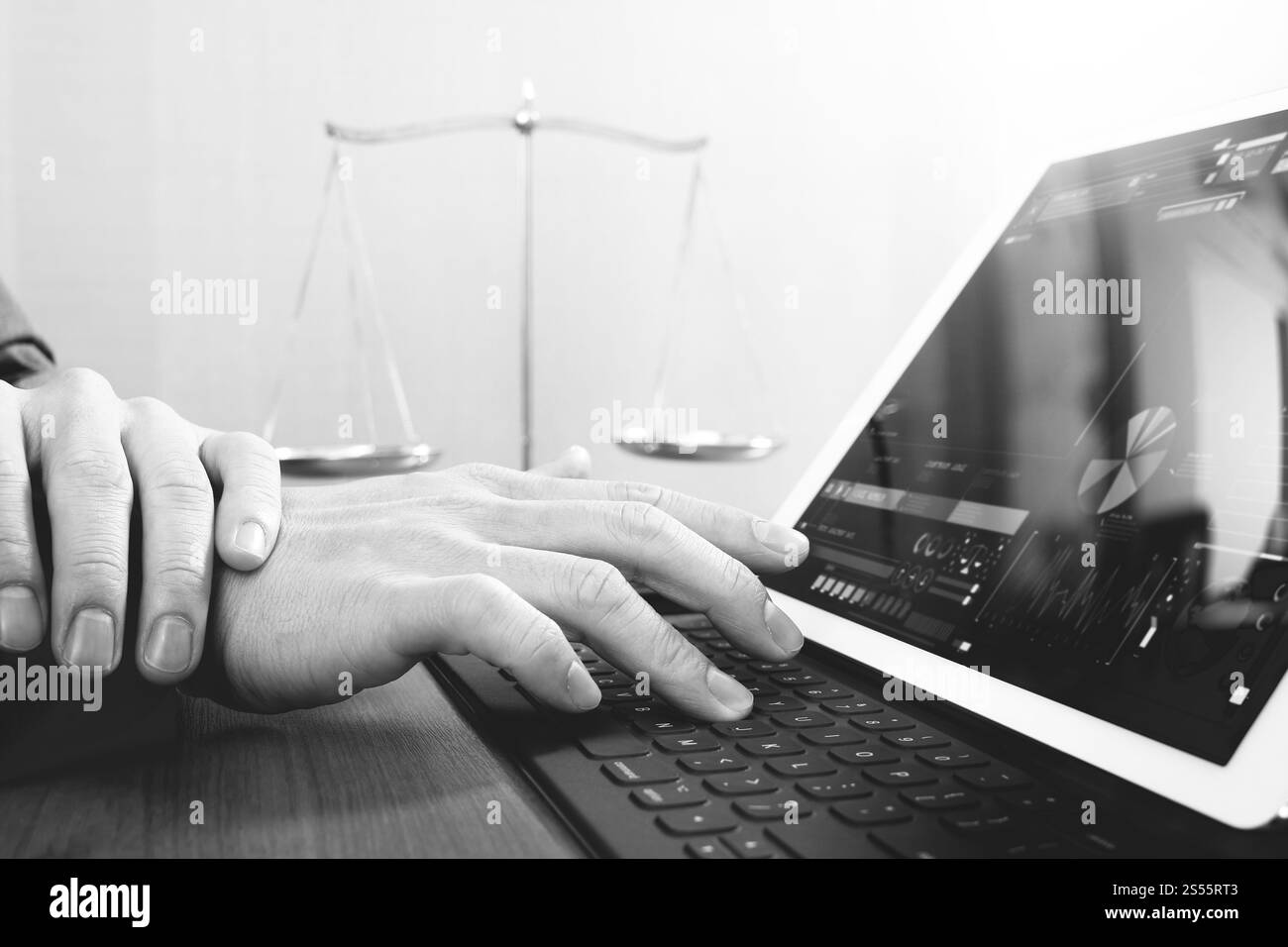 La giustizia e la nozione di diritto.avvocato maschio in ufficio con il martello,lavora con smart phone e digital computer tablet e scala di ottone su tavola di legno,nero Foto Stock