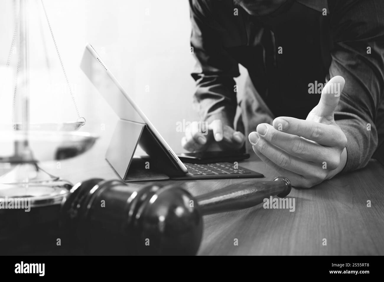 La giustizia e la nozione di diritto.avvocato maschio in ufficio con il martello,lavora con smart phone e digital computer tablet e scala di ottone su tavola di legno,nero Foto Stock