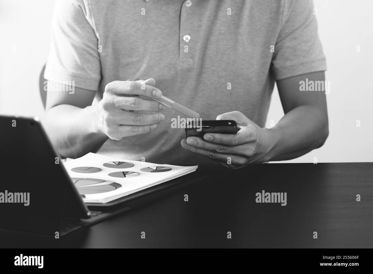 Imprenditore nel t-shirt rosa lavora con smart phone e tablet digitali computer sulla scrivania di legno in un ufficio moderno,in bianco e nero Foto Stock