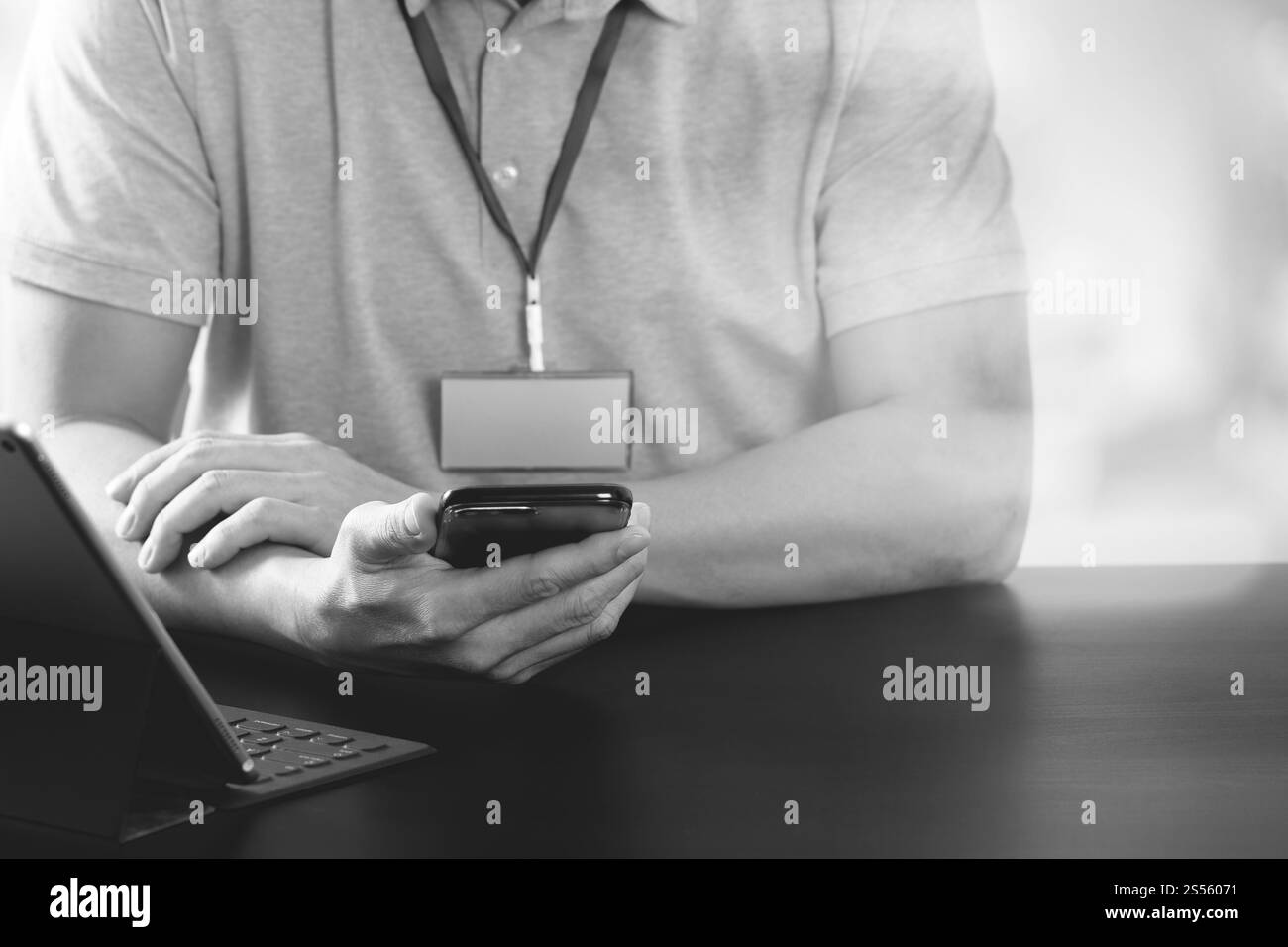 Imprenditore nel t-shirt rosa lavora con smart phone e tablet digitali computer sulla scrivania di legno in un ufficio moderno,in bianco e nero Foto Stock