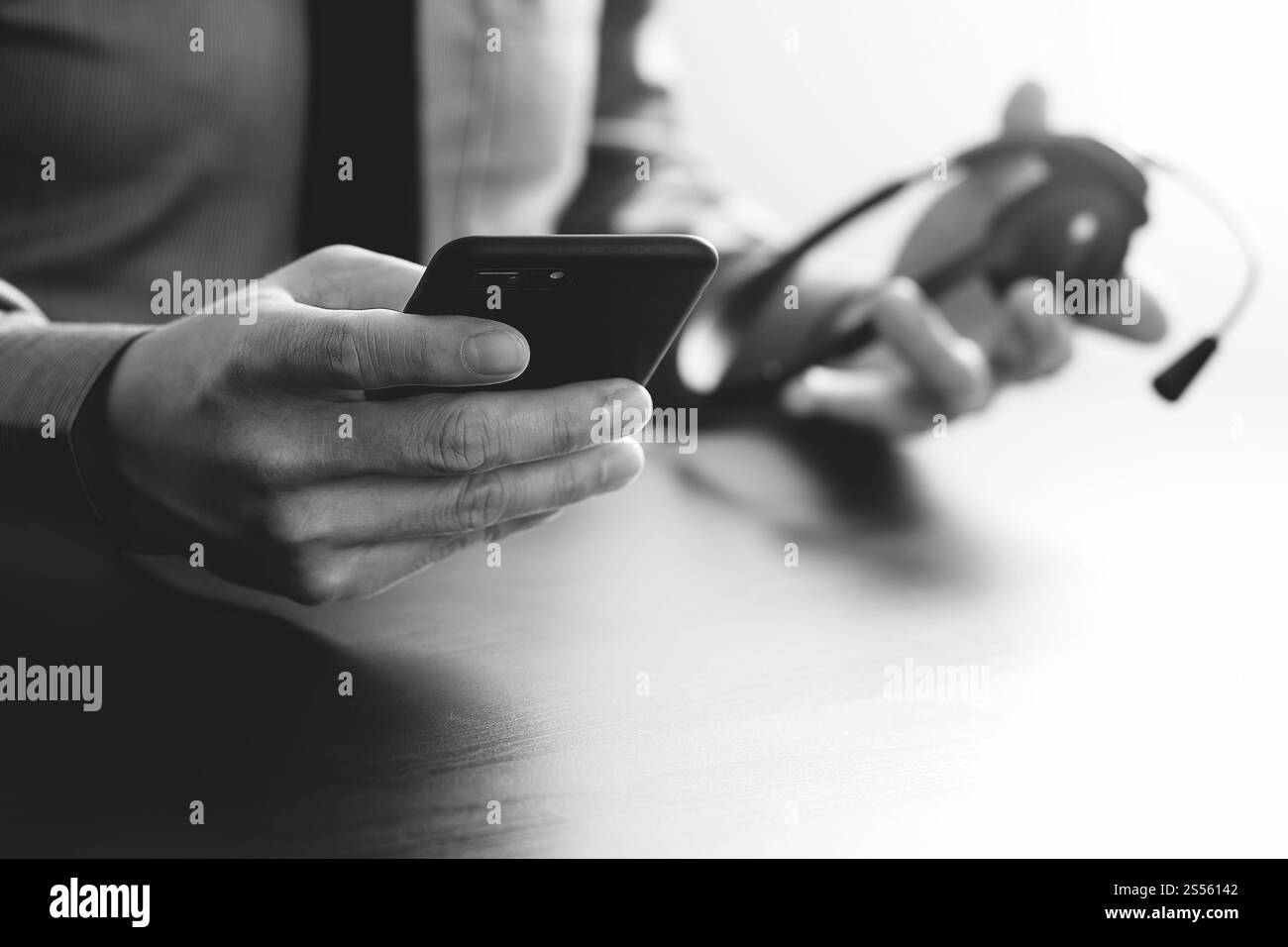 Imprenditore tramite VOIP auricolare con il telefono cellulare e il concetto di comunicazione centro di chiamata sulla scrivania in legno,in bianco e nero Foto Stock