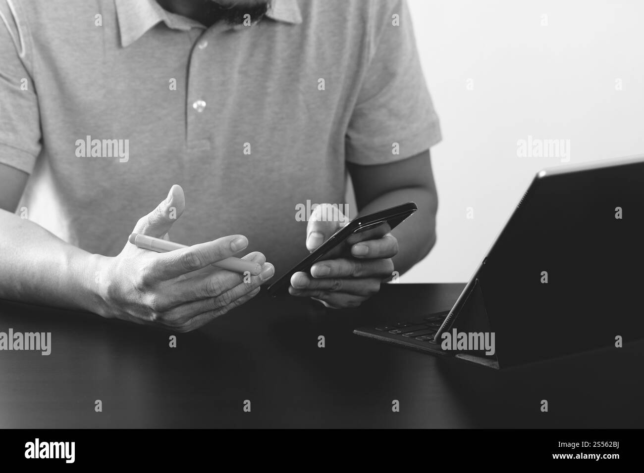 Imprenditore nel t-shirt rosa lavora con smart phone e tablet digitali computer sulla scrivania di legno in un ufficio moderno,in bianco e nero Foto Stock