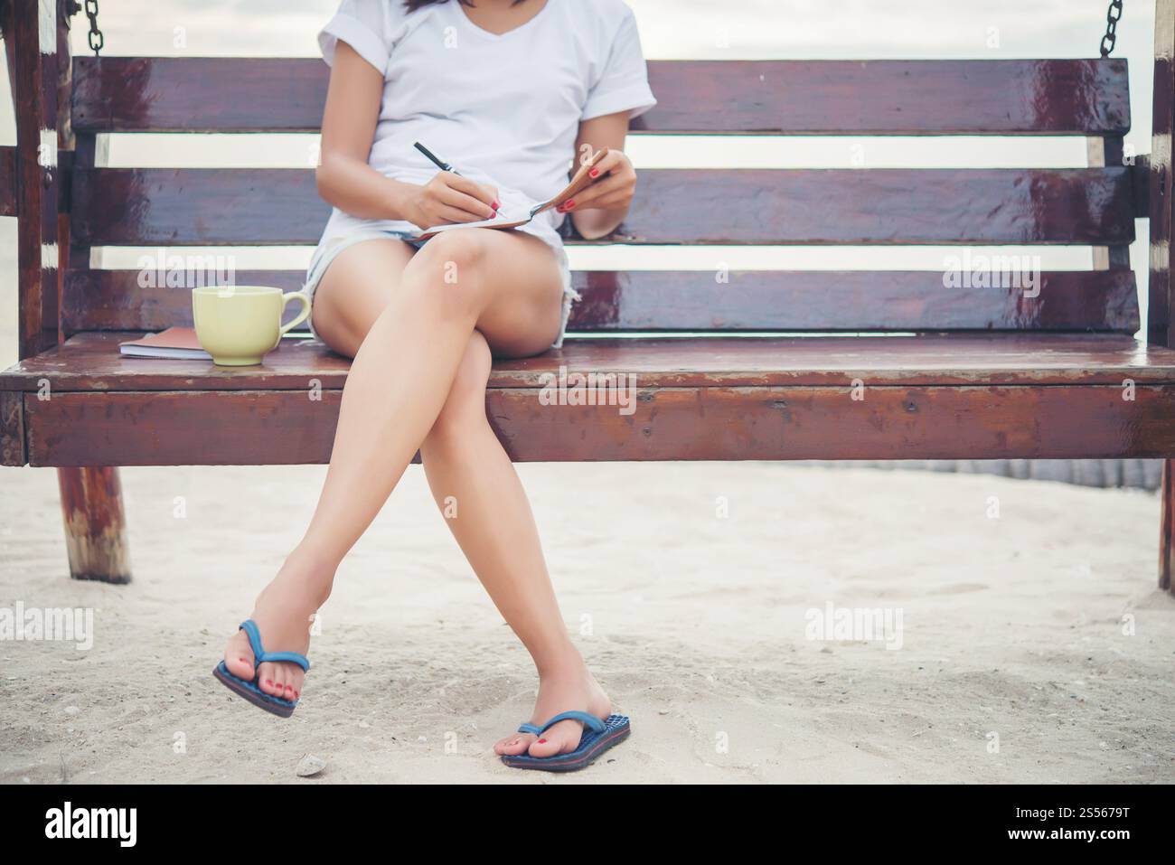 Giovane donna bella scrittura su notepad mentre è seduto sul banco di lavoro. Rilassarsi sulla spiaggia. Foto Stock