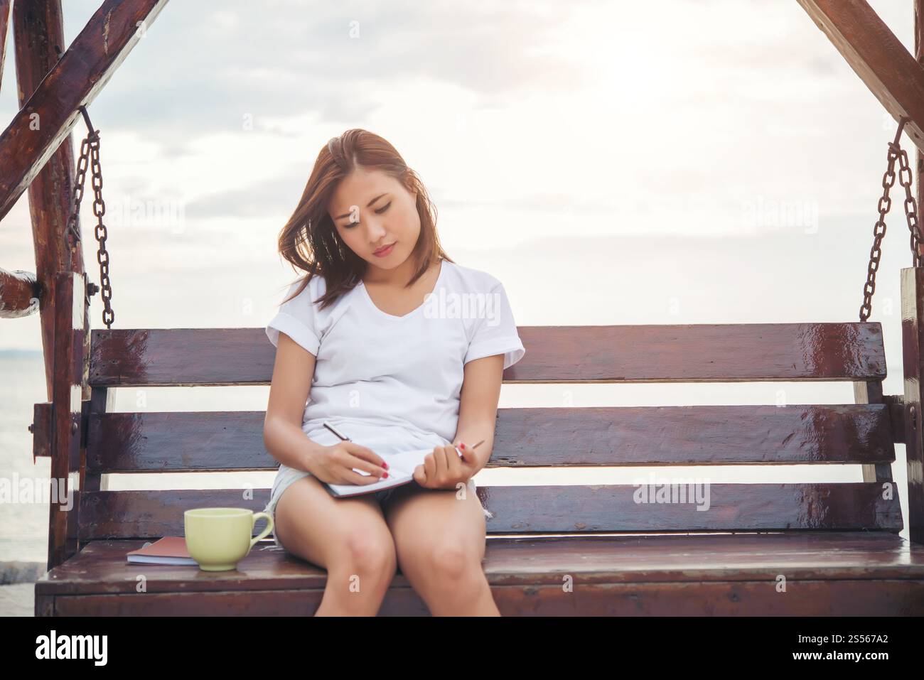 Giovane donna bella scrittura su notepad mentre è seduto sul banco di lavoro. Rilassarsi sulla spiaggia. Foto Stock