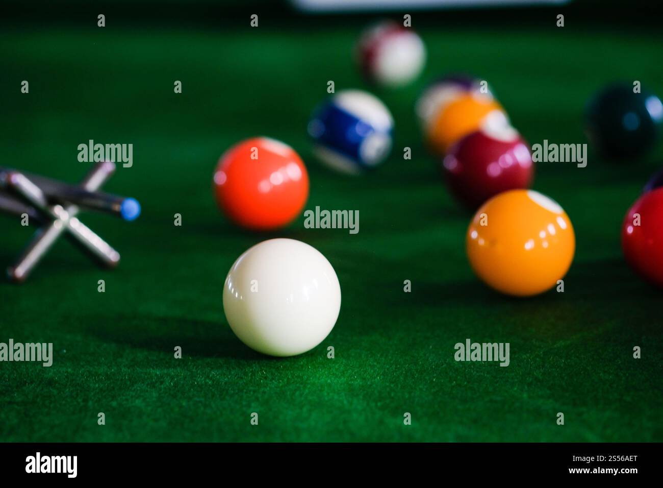 Mans mano e braccio cue giocano a biliardo o si preparano a sparare palle da biliardo su un tavolo da biliardo verde. Palline da biliardo colorate sul fregio verde Foto Stock