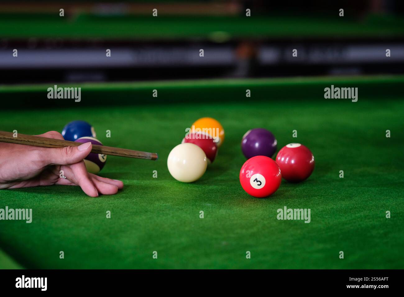 Mans mano e braccio cue giocano a biliardo o si preparano a sparare palle da biliardo su un tavolo da biliardo verde. Palline da biliardo colorate sul fregio verde Foto Stock