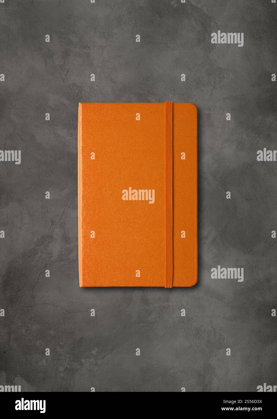 Mockup di notebook chiuso arancione isolato su sfondo di cemento scuro. Quaderno chiuso arancione su sfondo di cemento scuro Foto Stock