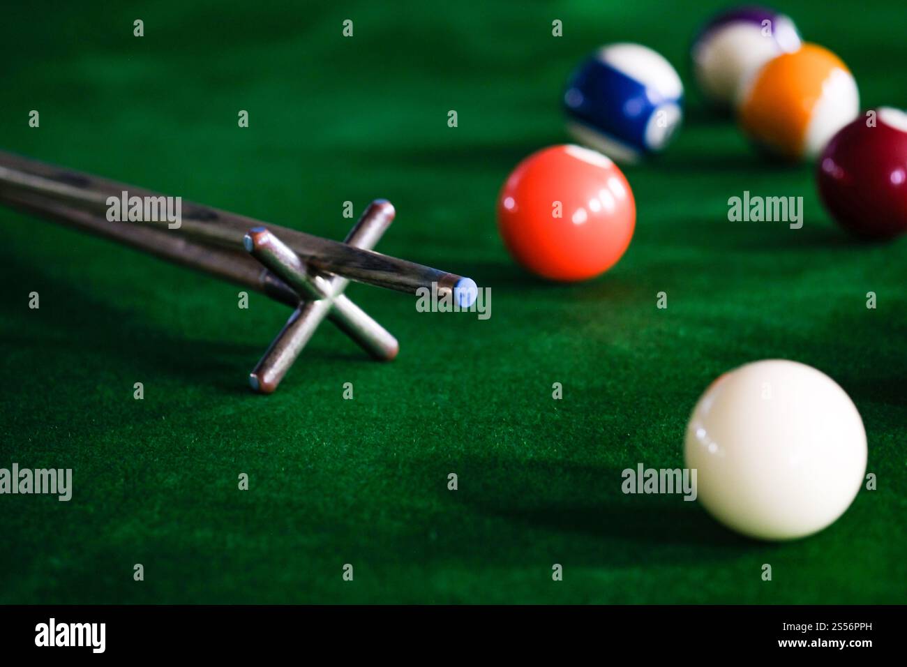 Mans mano e braccio cue giocano a biliardo o si preparano a sparare palle da biliardo su un tavolo da biliardo verde. Palline da biliardo colorate sul fregio verde Foto Stock