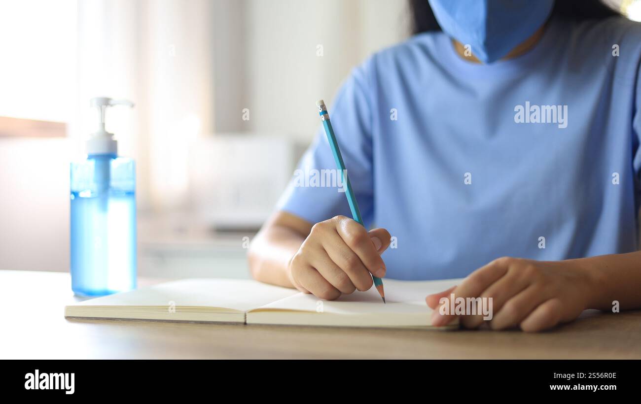 Giovane donna asiatica che indossa maschera facciale medica fatta a mano che lavora da sola distanziando politica con. Gel igienizzante per le mani durante il coronavirus o il virus covid-19 Foto Stock