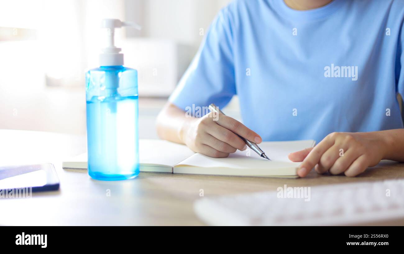 Giovane donna asiatica che indossa maschera facciale medica fatta a mano che lavora da sola distanziando politica con. Gel igienizzante per le mani durante il coronavirus o il virus covid-19 Foto Stock