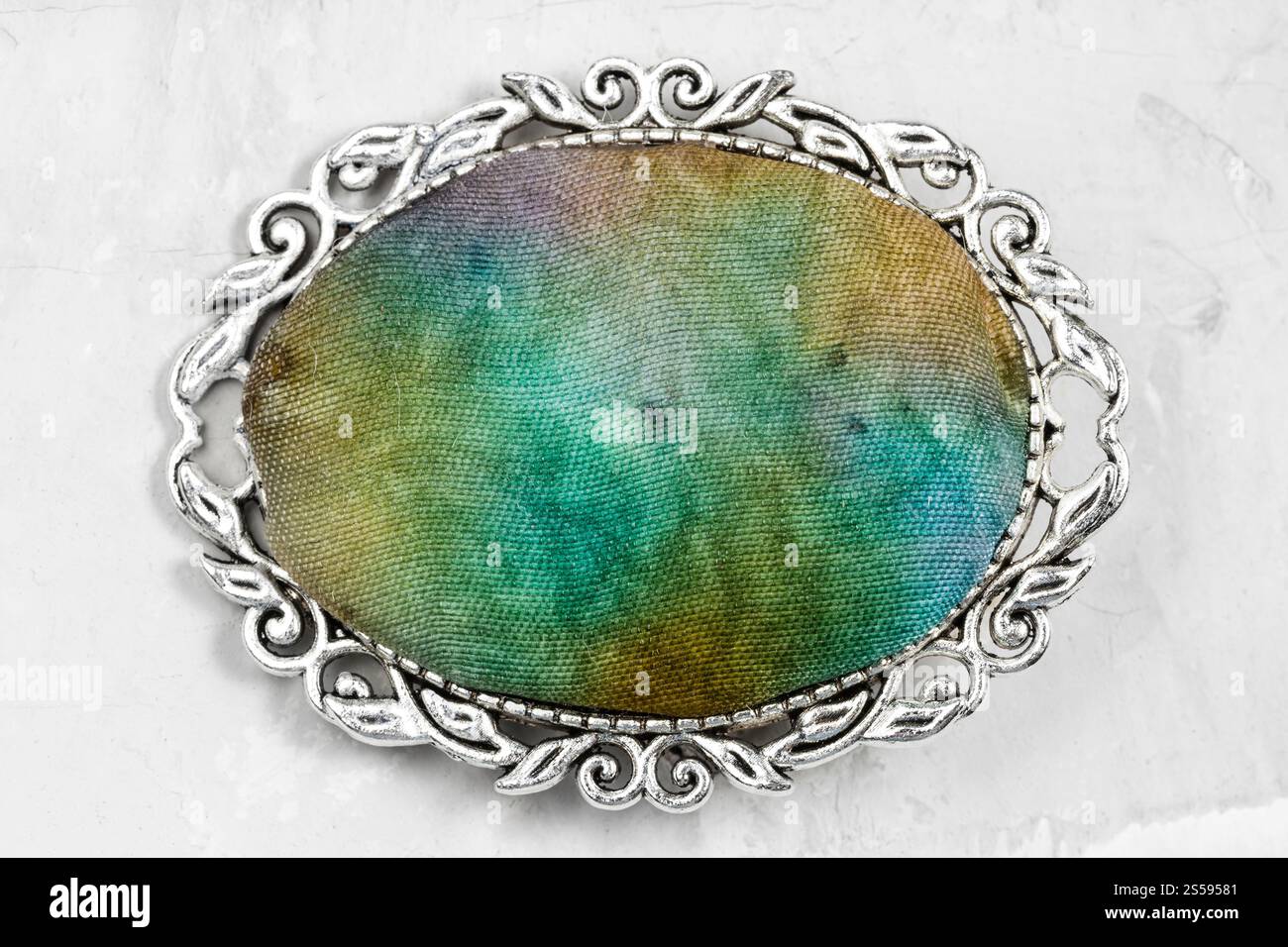 spilla ovale in argento con inserto in seta batik colorato a mano su pannello in calcestruzzo grigio Foto Stock
