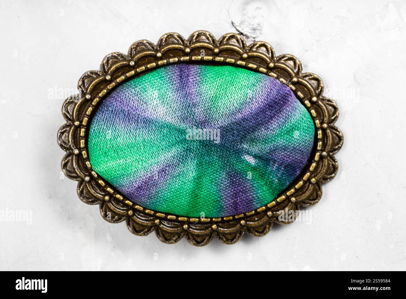 spilla ovale in bronzo con inserto in seta batik colorato a mano su pannello in calcestruzzo grigio Foto Stock