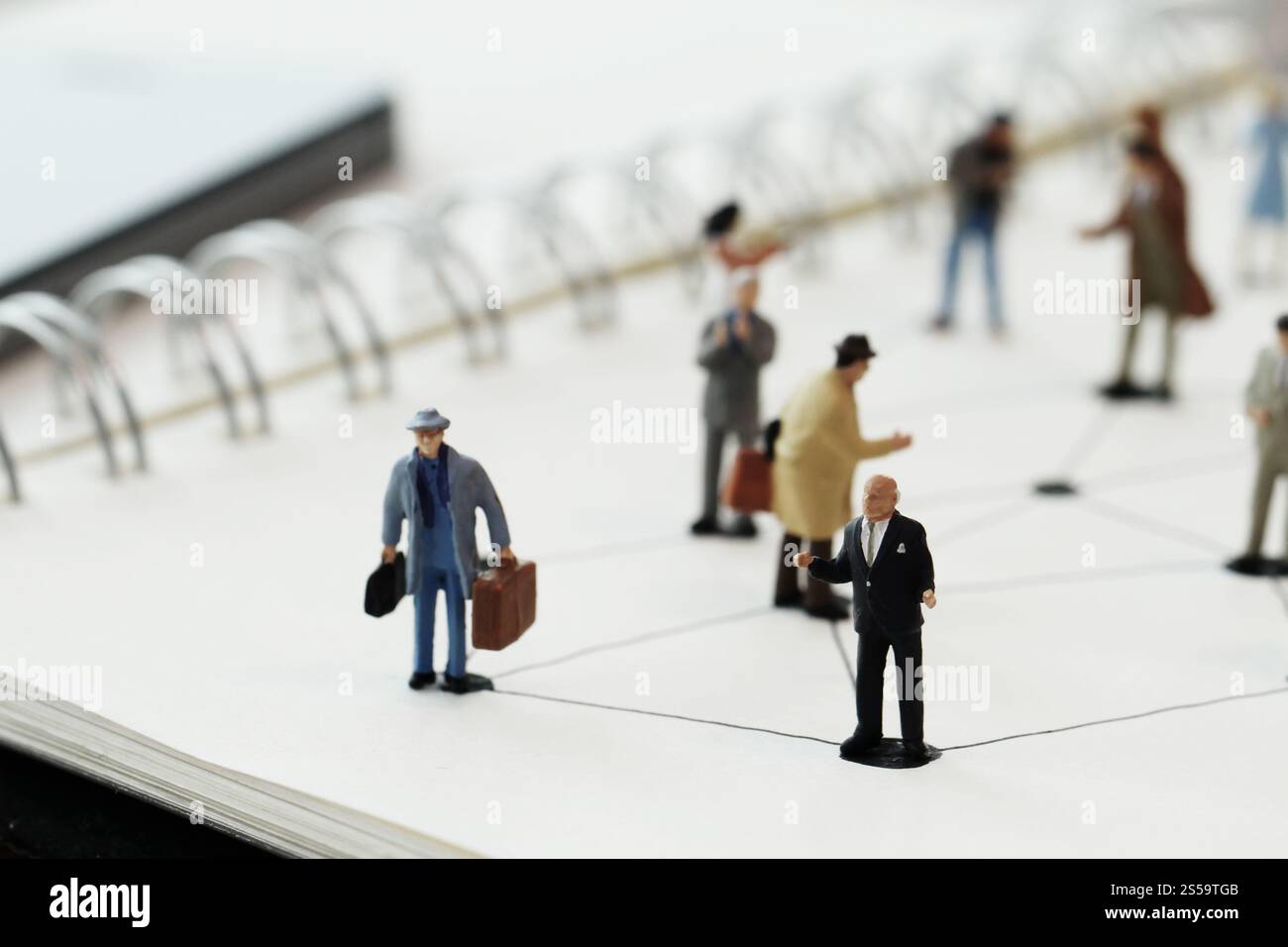 primo piano di persone in miniatura con un diagramma di social network su un notebook aperto su una scrivania in legno mentre i social media si avvicinano Foto Stock