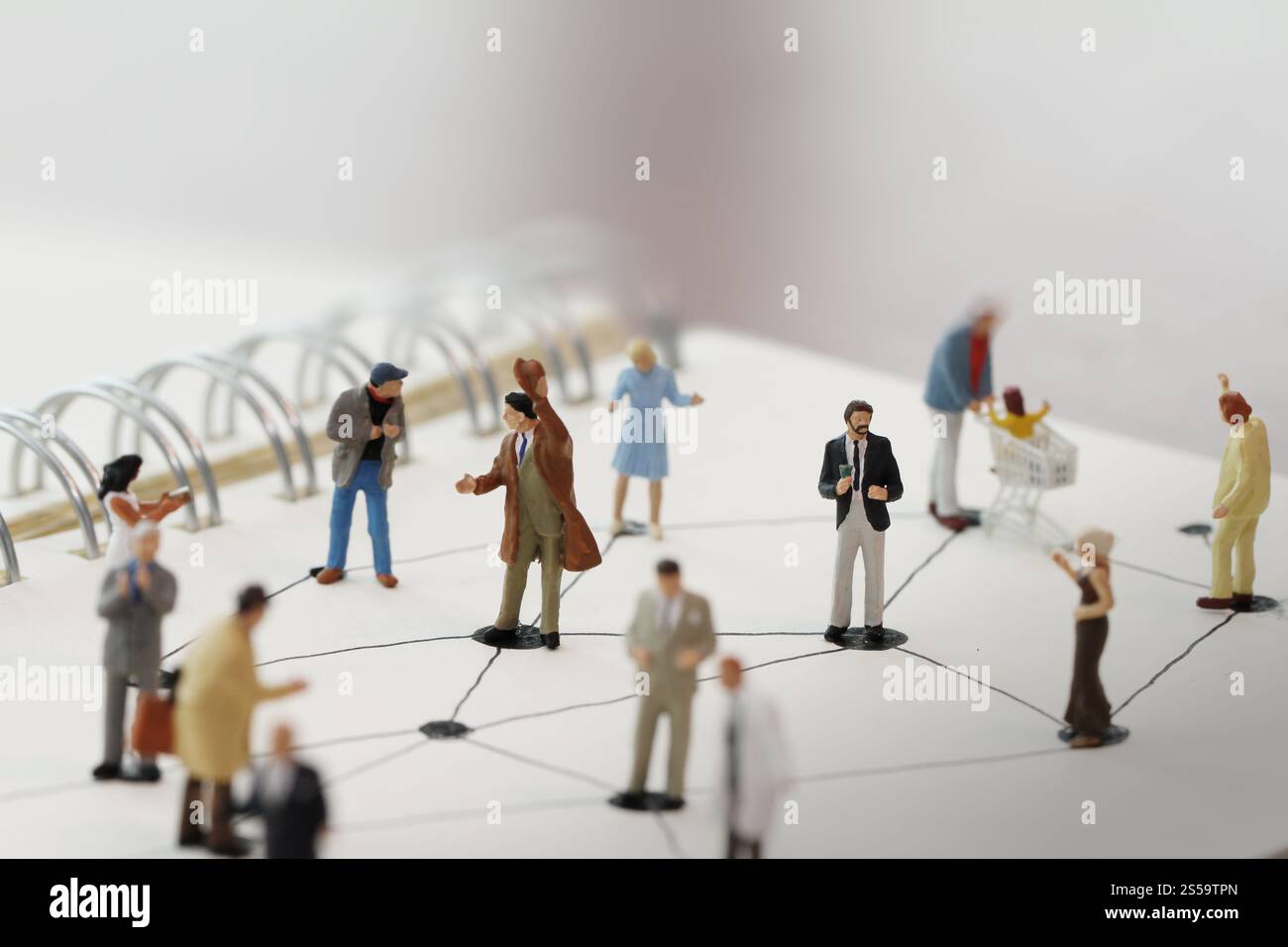 primo piano di persone in miniatura con un diagramma di social network su un notebook aperto su una scrivania in legno mentre i social media si avvicinano Foto Stock