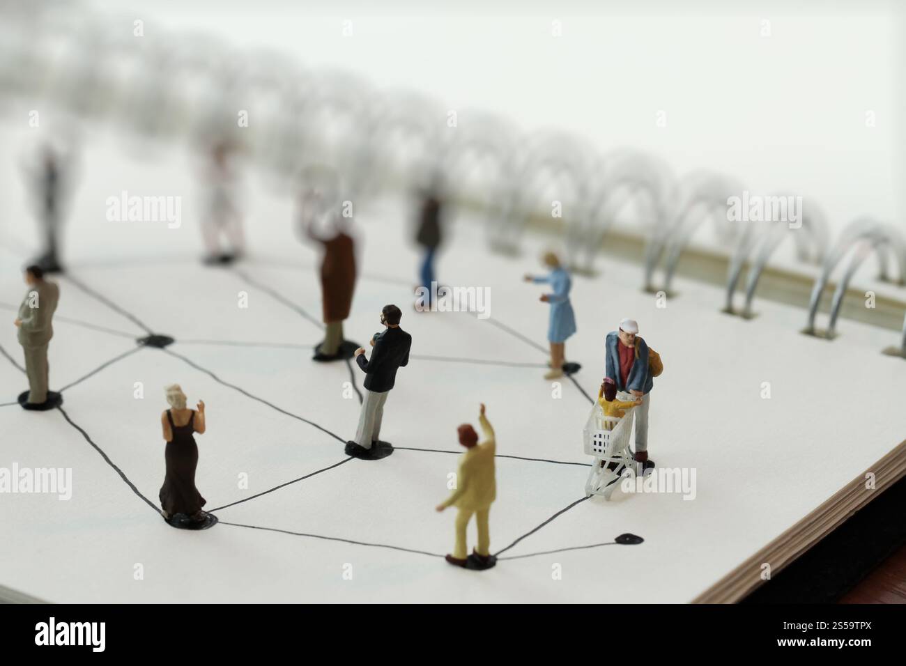 primo piano di persone in miniatura con un diagramma di social network su un notebook aperto su una scrivania in legno mentre i social media si avvicinano Foto Stock